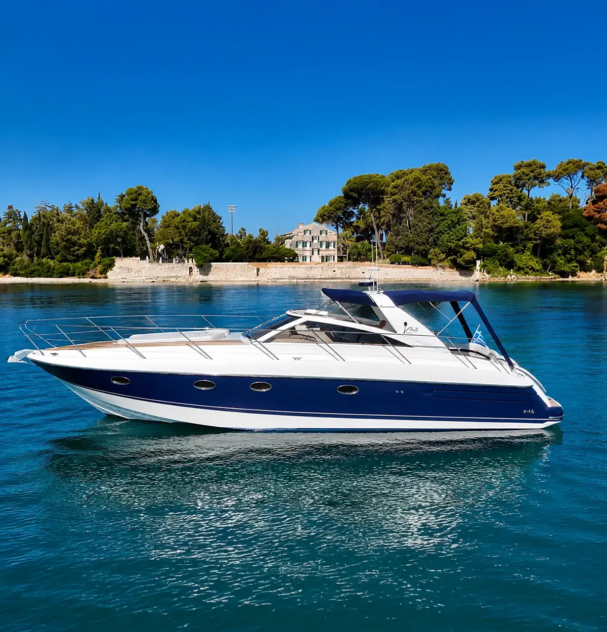 White and navy luxury motor yacht on calm blue water with a tree-lined shore in the background, under a clear sky.